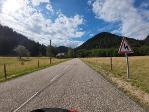 Eine Landstraße schlängelt sich unter einem bewölkten Himmel durch malerische Felder und Hügel, perfekt für geführte Motorradtouren.