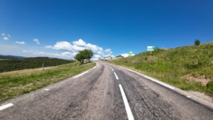 Eine malerische Landstraße schlängelt sich durch üppige Hügel, perfekt für geführte Motorradtouren, mit Schildern und Gebäuden.