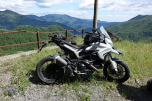 Ein Motorrad auf einer Hügelkuppe mit Blick auf üppige Berge und einen teilweise bewölkten Himmel, perfekt für geführte Touren.