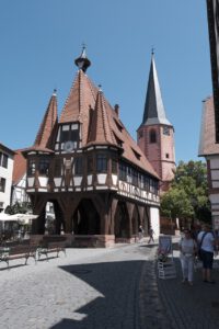 Ein charmantes Fachwerkgebäude mit rotem Dach ziert einen belebten, mit Kopfstein gepflasterten Platz, auf dem die Menschen ihre Erkundungstouren unternehmen können.