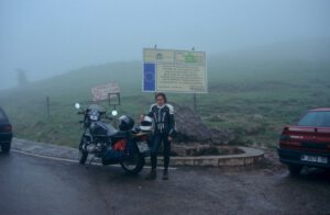 Ein Biker in voller Montur steht mit seinem Motorrad auf einer nebligen Straße und lädt zu abenteuerlichen geführten Motorradtouren ein.