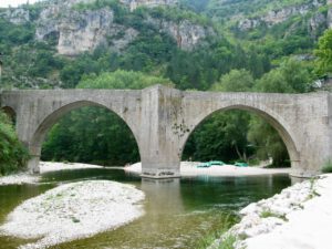 Eine steinerne Bogenbrücke überspannt einen ruhigen Fluss mit grünen Kanus am Ufer, perfekt für geführte Motorradtouren.