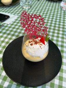 Eine dekadente Mousse im Glas, garniert mit Schlagsahne, Schokolade und Erdbeere auf einem schicken schwarzen Teller.