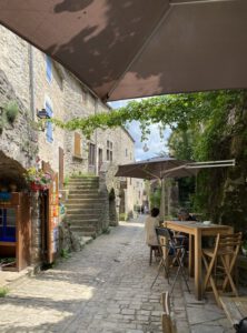 Eine charmante Kopfsteinpflasterstraße mit rustikalen Steingebäuden, Sitzgelegenheiten im Freien, Weinreben und leuchtenden Blumen.