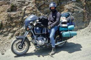 Ein für ein Abenteuer gerüsteter Fahrer eines BMW-Motorrads hält auf einer Schotterstraße an einem felsigen Hang an.