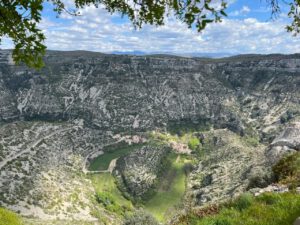 Ein malerisches grünes Tal mit Klippen, einem kleinen Dorf und gewundenen Wegen, ideal für geführte Motorradreisen.