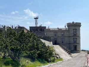 Bei klarem Himmel bilden ein burgähnliches Steingebäude und üppiges Grün einen perfekten Aussichtspunkt.