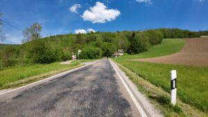 Eine Landstraße führt zu einem Haus inmitten üppiger Felder und Bäume, ideal für geführte Motorradtouren.