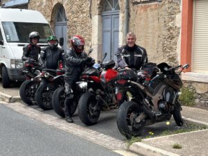 Vier Motorradfahrer in voller Montur machen auf einer Kopfsteinpflasterstraße neben ihren Motorrädern eine Pause und versprühen den Charme dieser Tour.