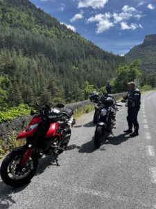 Zwei Motorradfahrer genießen eine Pause inmitten üppigen Grüns und blauen Himmels auf einer malerischen Bergstraße.