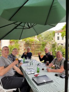 Fünf Freunde stoßen unter einem grünen Schirm an einem karierten Tisch fröhlich an und genießen ihre Motorradtour-Pause.
