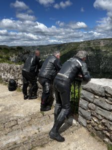 Drei Motorradfahrer in schwarzer Montur planen ihren nächsten Stopp und genießen die Aussicht von einem Hügel unter einem teilweise bewölkten Himmel.