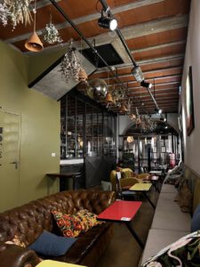Gemütliches Café mit Ledersofas, geblümten Kissen und Hängepflanzen; perfekt für die Planung Ihres nächsten Abenteuers.