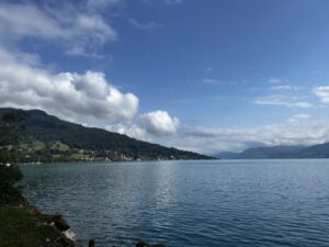 Ein ruhiger See mit grünen Hügeln und einer malerischen Stadt, ideal für geführte Motorradtouren inmitten ferner Berge.