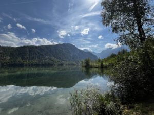 In einem ruhigen See spiegeln sich Berge und Wolken wider, und die sonnenbeschienenen Ufer eignen sich perfekt für geführte Motorradtouren.