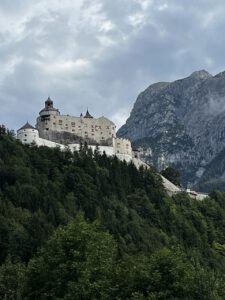 Entdecken Sie eine majestätische Burg auf einem Hügel, umgeben von Wäldern und Bergen, ideal für geführte Motorradtouren.
