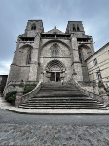 Ein Reisender steigt unter bewölktem Himmel die große Treppe einer historischen Steinkathedrale hinauf.