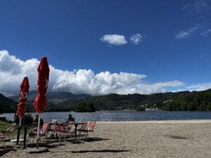 Eine ruhige Lage am Seeufer mit roten Sonnenschirmen, leeren Tischen und einem Biker, der die malerische Hügel und den See genießt.