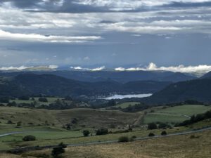 Sanfte grüne Hügel, kurvenreiche Straßen, ideal für Motorradtouren, ein See und neblige Berge.