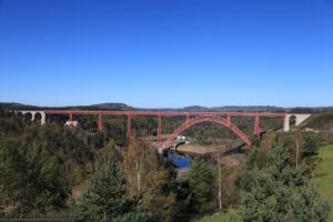 Eine atemberaubende rote Bogenbrücke überspannt einen Fluss, eingebettet in üppig grüne Hügel – perfekt für geführte Motorradtouren.