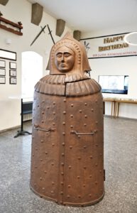Eine rostige Eiserne Jungfrau, ein mittelalterliches Foltergerät, steht in einem Museumsraum mit historischen Ausstellungsstücken in der Nähe.