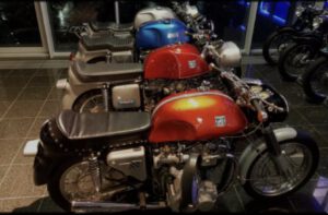 Vintage-Motorräder mit Chromverzierungen und bunten Tanks glänzen auf dem glänzenden Boden eines Ausstellungsraums.