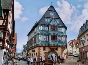 Ein charmantes Fachwerkhaus mit blauen Akzenten in einer Kopfsteinpflasterstraße, in der es von Menschen wimmelt.