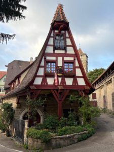 Charmantes Fachwerkhaus mit roten Balken, Steildach, Blumenkästen und einem blühenden Vorgarten.