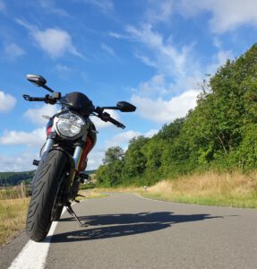 Ein schwarzes Motorrad steht auf einer Landstraße unter blauem Himmel, flankiert von grünen Bäumen und Gras.