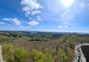 Panoramablick auf üppig grüne Hügel und Wälder unter blauem Himmel, von oben gesehen mit Steingeländer.