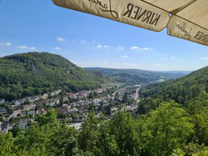 Eine grüne Talstadt mit bewaldeten Hügeln, blauem Himmel und einem KIRNER-Schirm, der oben rechts zu sehen ist.