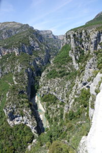 Üppig grüne Klippen ragen über einen sich schlängelnden Fluss in einer tiefen Schlucht empor, und das alles unter einem strahlend blauen Himmel.