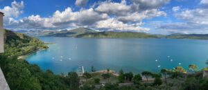 Ein blauer See mit Booten, umgeben von grünen Hügeln und Bergen unter einem teilweise bewölkten Himmel.