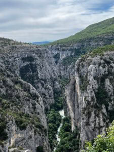 Eine enge Schlucht mit steilen Felswänden, üppiger Vegetation und einem sich schlängelnden Fluss unter einem bewölkten Himmel.