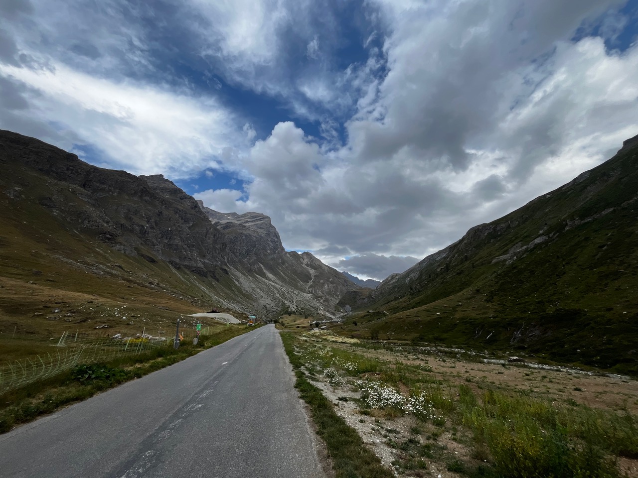 IMG_7500 Eine schmale, asphaltierte Straße schlängelt sich durch ein üppig bewachsenes Bergtal unter einem dramatischen, wolkenverhangenen Himmel.