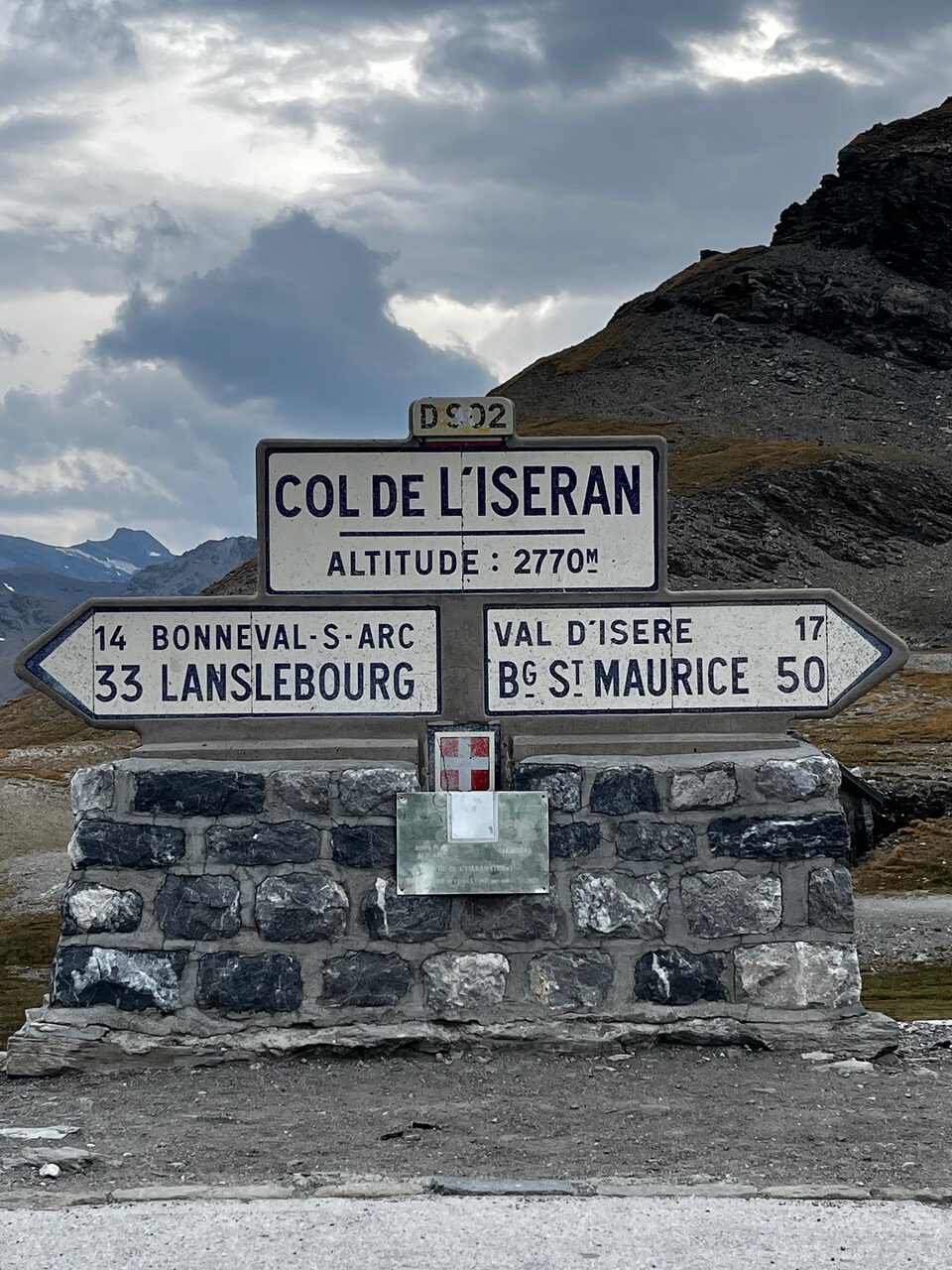 IMG_7510 Steinschild am Col de l’Iseran, 2770 m, mit Richtungspfeilen und Bergen im Hintergrund.