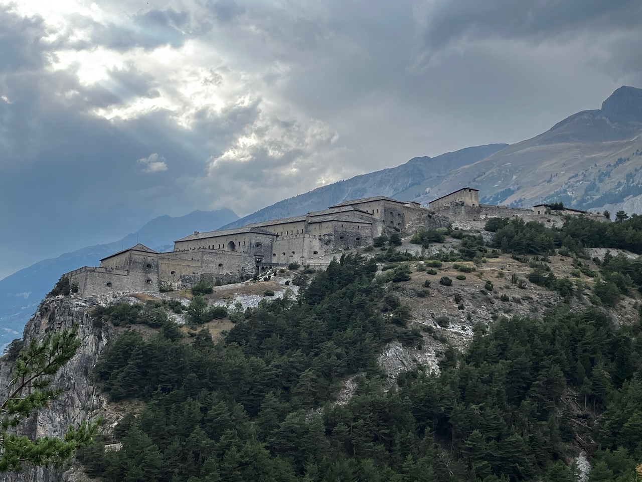 IMG_7525 Eine gewaltige Steinfestung thront auf einem bewaldeten Bergrücken unter den Wolken, dahinter erheben sich weitere Gipfel.