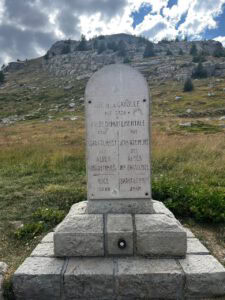 Steinmarkierung am Col de la Cayolle mit Angaben zu Höhe, Grenzen und Entfernungen; dahinter ein felsiger Hang.