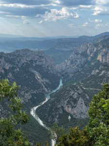 Ein gewundener, türkisfarbener Fluss schlängelt sich unter einem teilweise bewölkten, dunstigen Himmel durch die Felsen einer üppig bewachsenen Schlucht.
