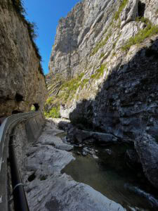 Ein schmaler Fluss schlängelt sich durch eine felsige Schlucht unter hohen Klippen hindurch, begleitet von einem mit Geländern gesäumten Weg und einem strahlend blauen Himmel.