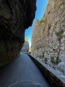 Eine kurvenreiche, asphaltierte Straße schlängelt sich zwischen hoch aufragenden Felsklippen unter strahlend blauem Himmel und in der Sonne hindurch.