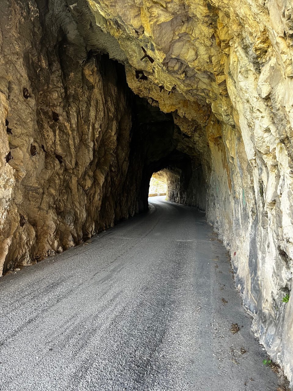 IMG_7684 Eine schmale, asphaltierte Straße schlängelt sich durch einen zerklüfteten Felsentunnel, an dessen fernem Ausgang Licht scheint.