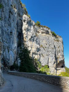 Eine kurvenreiche Straße schlängelt sich an einer hohen, felsigen Klippe entlang, die unter dem strahlend blauen Himmel mit grünen Flecken übersät ist.